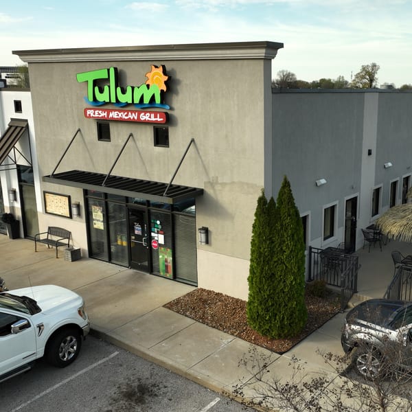 Exterior of Tulum Fresh Mexican Grill, a gray building with a vibrant green and orange sign, and outdoor seating.