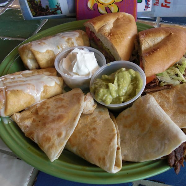 A green plate filled with Mexican food, including burritos, quesadillas, a torta, guacamole, and sour cream.