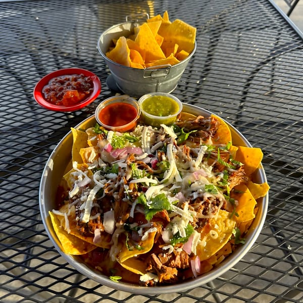 Tulum Fresh Mexican Grill's loaded nachos with meat, cheese, onions, cilantro, and salsas on a metal table.