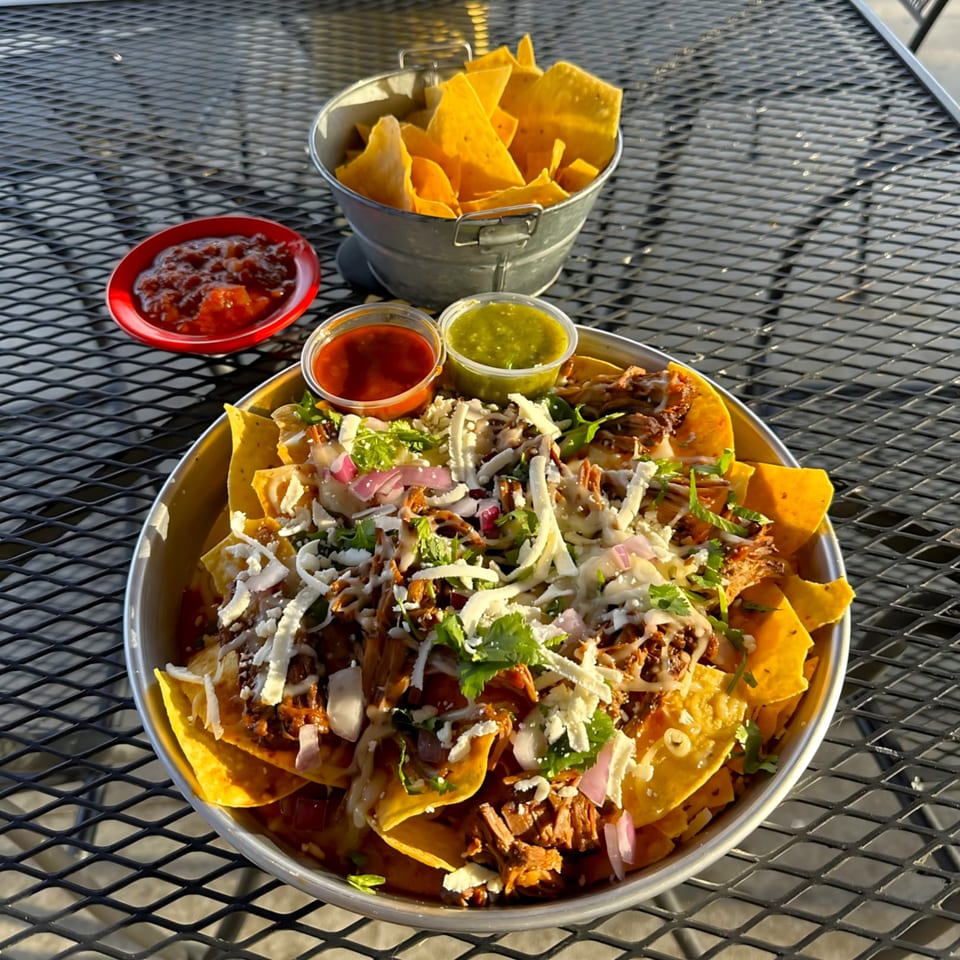 Tulum Fresh Mexican Grill's loaded nachos with meat, cheese, onions, cilantro, and salsas on a metal table.