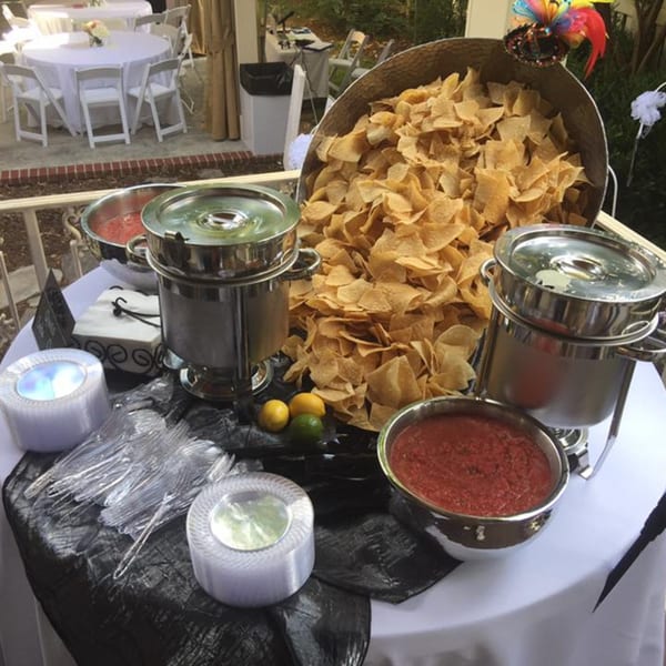 A buffet table with a large bowl of tortilla chips, salsa, and chafing dishes.