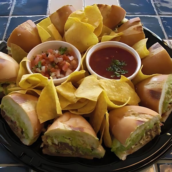 Mexican torta sandwiches, tortilla chips, salsa, and pico de gallo on a black platter.