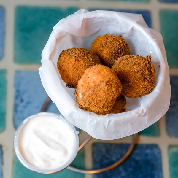 Crispy, golden-brown Mexican croquettes in a white paper-lined basket with a side of creamy dip.