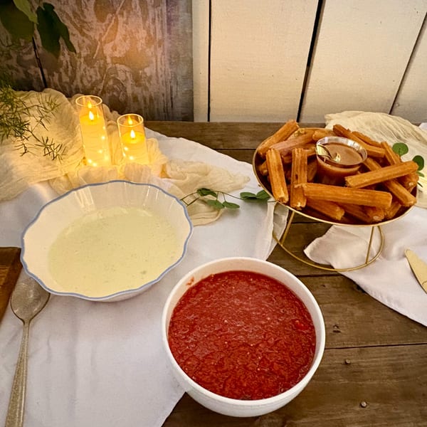 Churros with two dipping sauces and candles on a rustic wooden table.