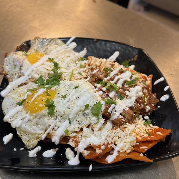 Chilaquiles with two fried eggs, shredded meat, cheese, cilantro, and crema on a black plate.