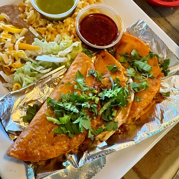 Three Tulum Fresh Mexican Grill birria tacos with cilantro, rice, beans, and two dipping sauces.