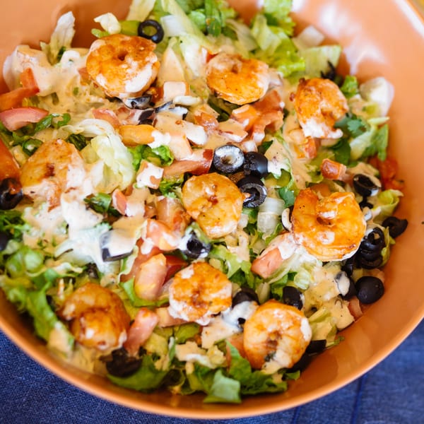 Shrimp salad with lettuce, tomatoes, black olives, and creamy dressing in an orange bowl.