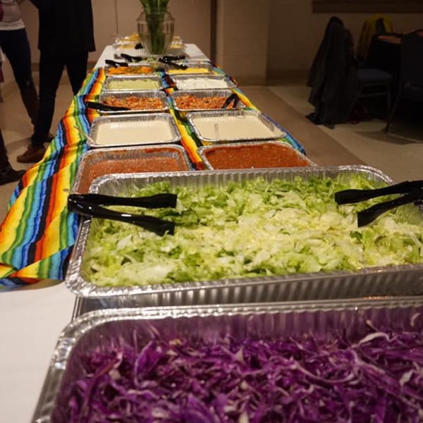 Mexican buffet with various toppings in foil pans, including shredded lettuce and purple cabbage.
