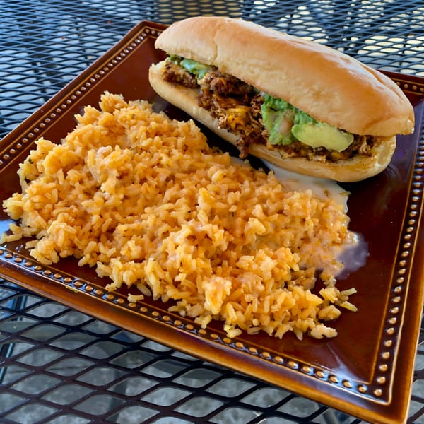 A Tulum Fresh Mexican Grill torta with avocado and rice on a brown plate.
