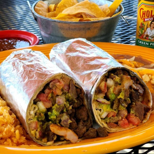 Two foil-wrapped burritos with rice and beans on a yellow plate, with chips and salsa.